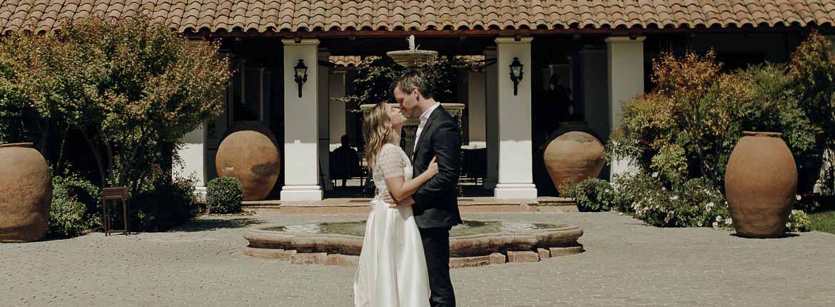 The bride and groom are kissing in front of the vineyard entrance