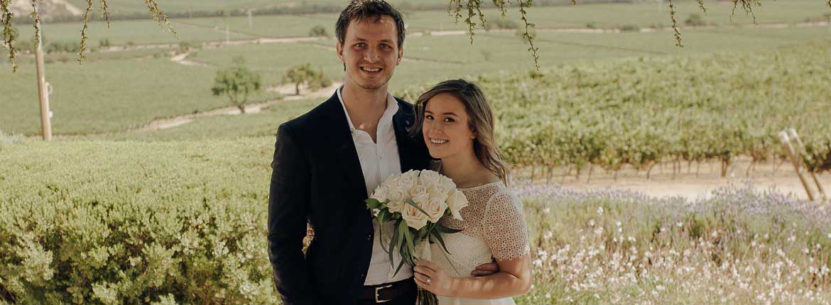 Bride and Groom are together, side by side, the bride holds the bouquet of white roses