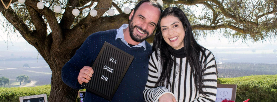 Casal feliz e Jean segura uma placa com a frase "ela disse sim"